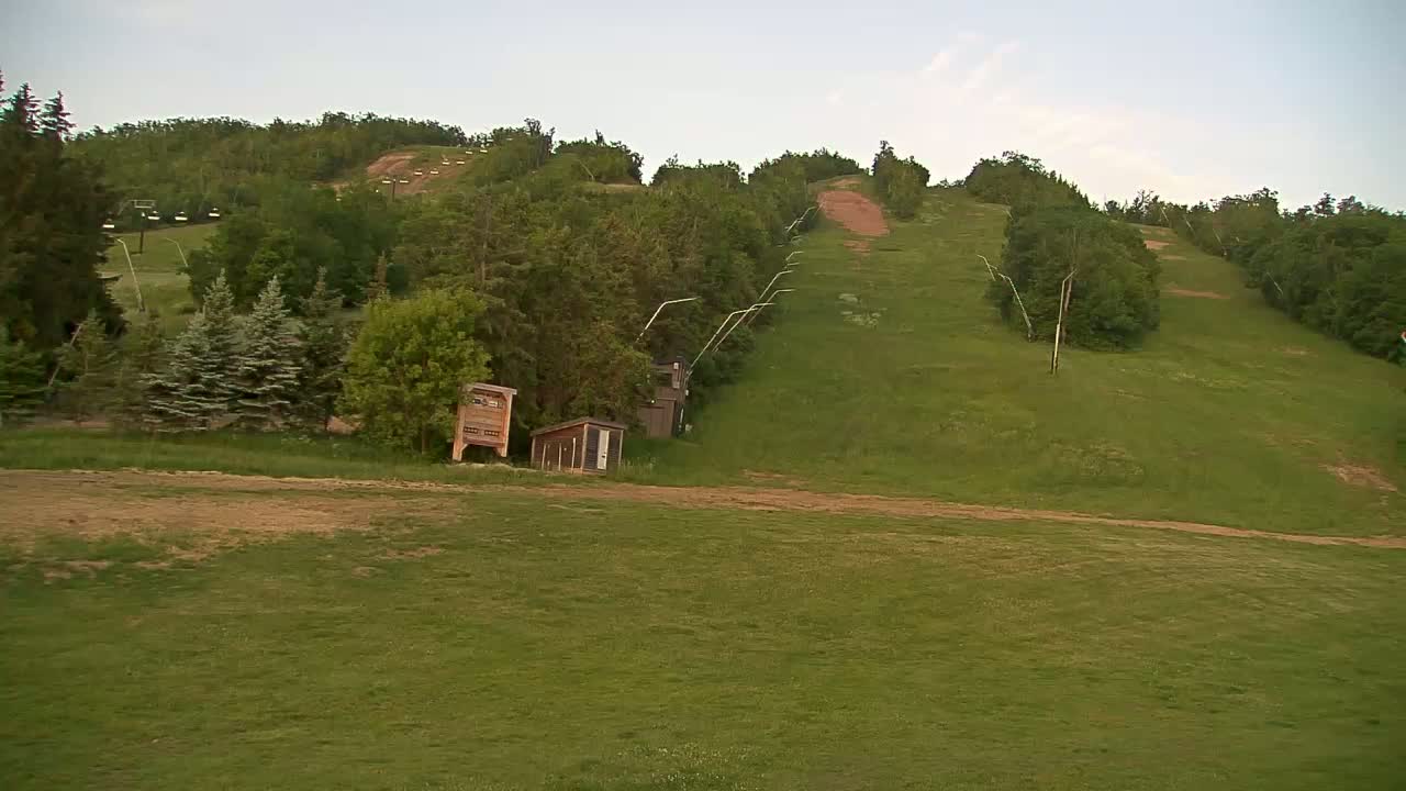 A grassy hill with a ski lift and small buildings under a mostly clear sky.