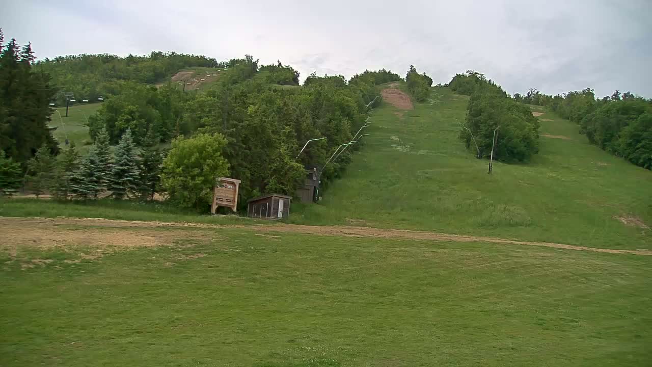 A grassy hillside with a ski lift and small buildings, under an overcast sky.