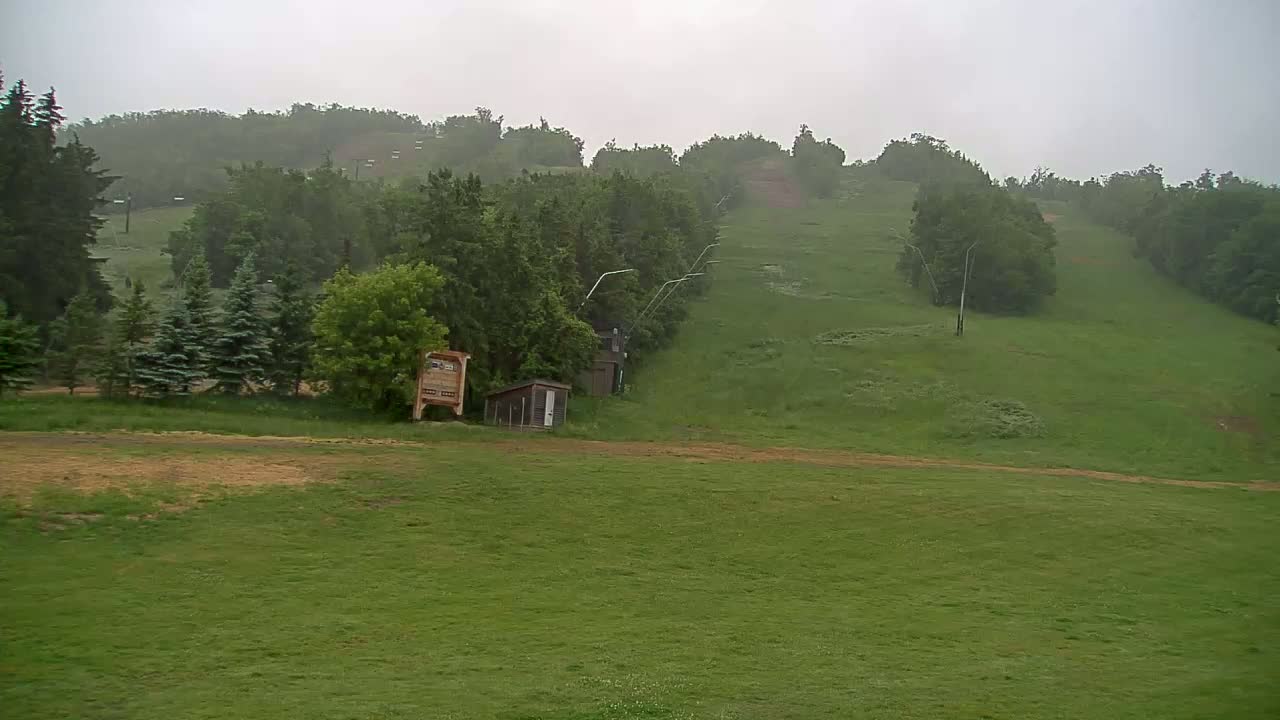 A grassy hillside with a chairlift and small buildings is visible under an overcast sky.