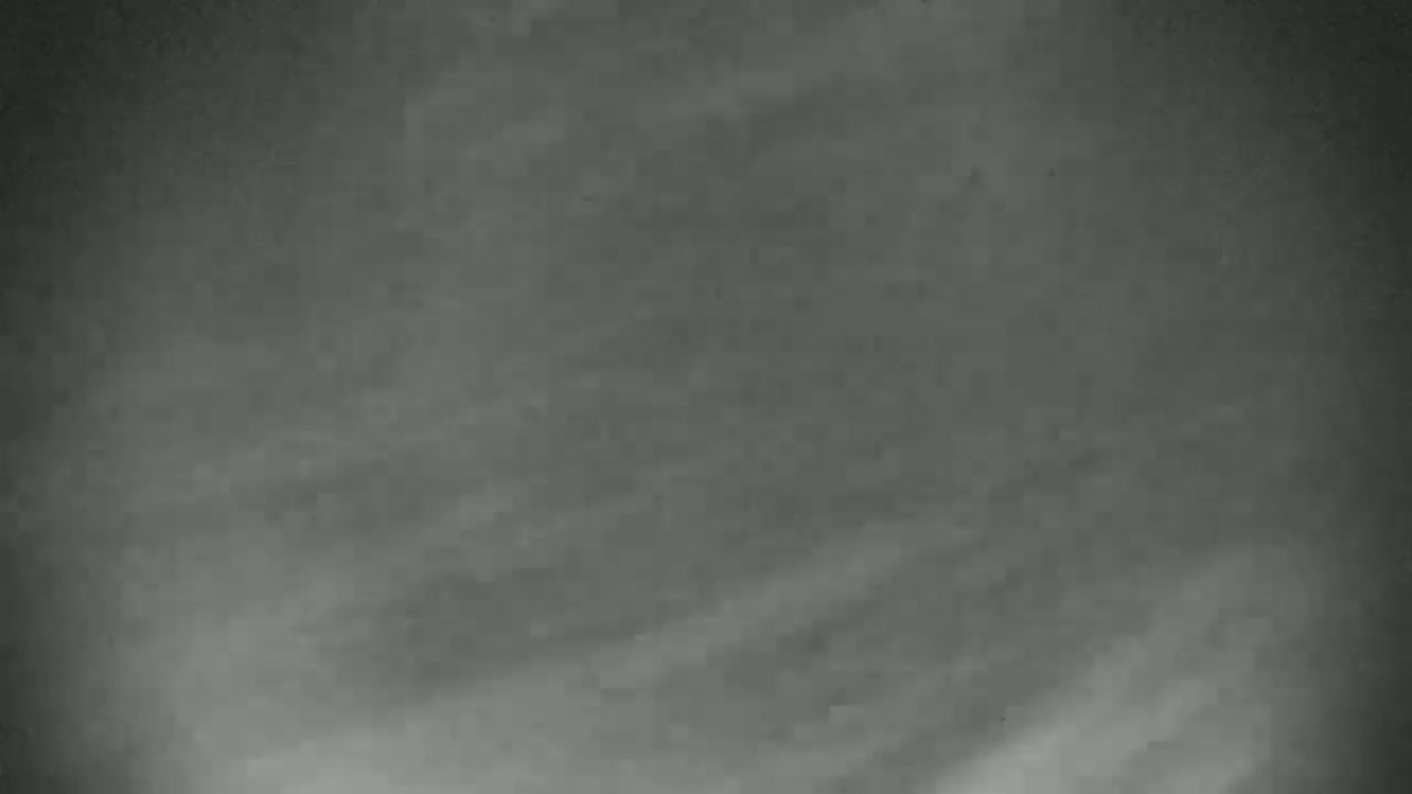 A grainy, monochrome image shows a cloudy, overcast sky.