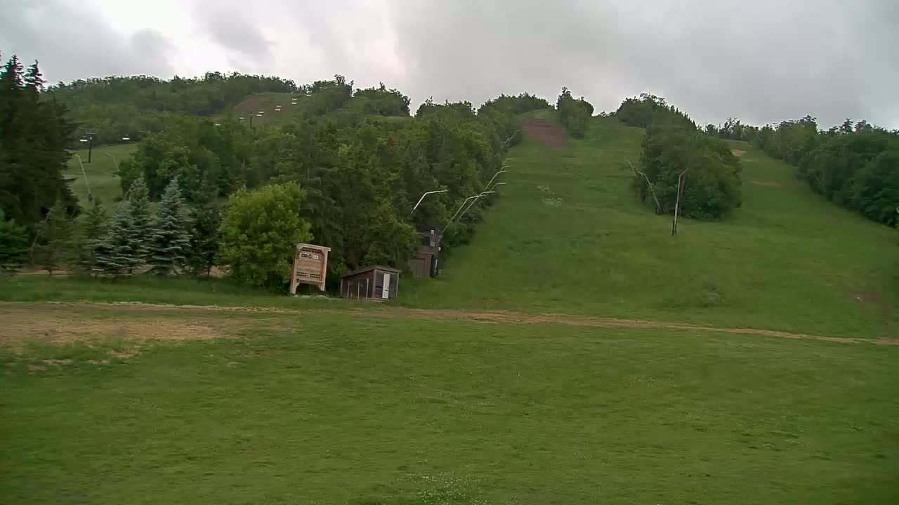 A grassy hillside with a ski lift and small buildings is visible under an overcast sky.