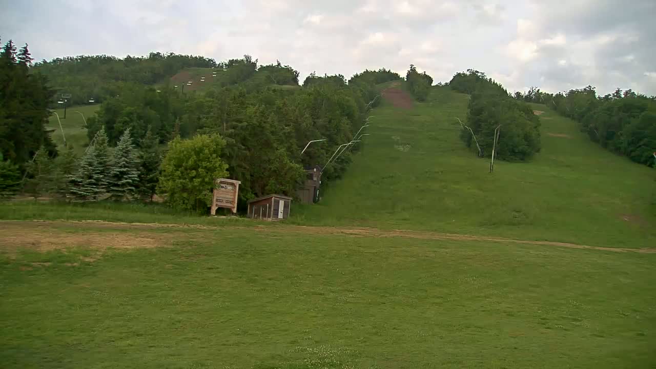 A grassy hill with a ski lift and several small buildings under a cloudy sky.