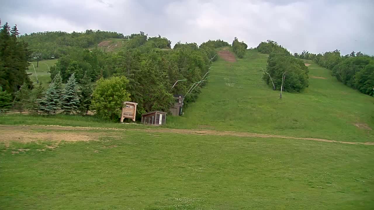 A grassy hillside with a ski lift and small buildings under a cloudy sky.