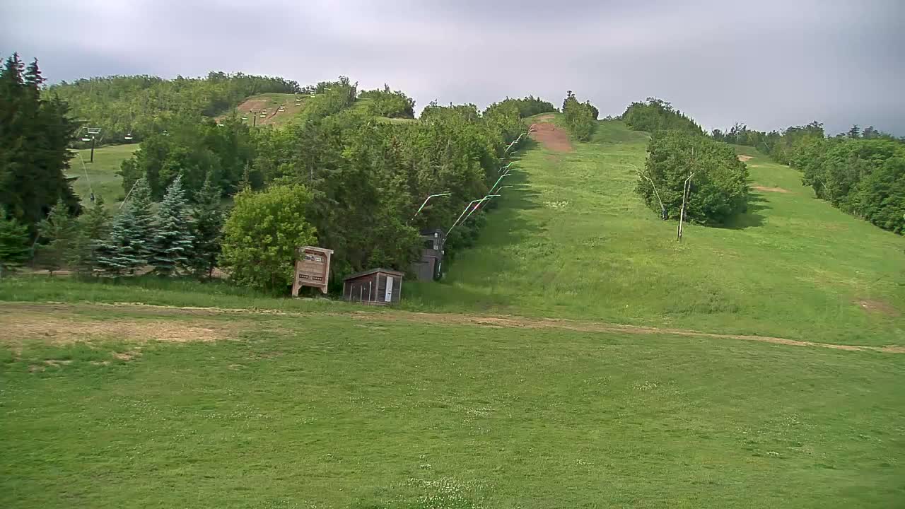 A grassy hillside with a chairlift and small buildings under a cloudy sky.