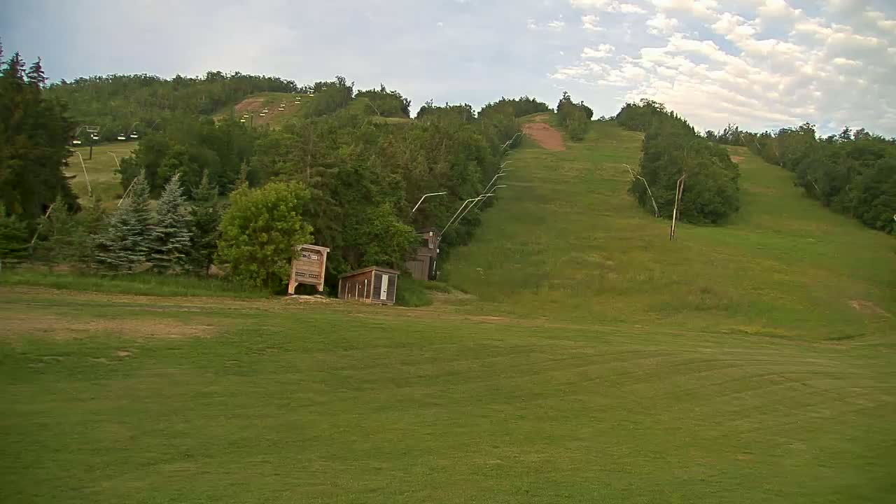 A grassy hillside with a chairlift and small buildings under a partly cloudy sky.