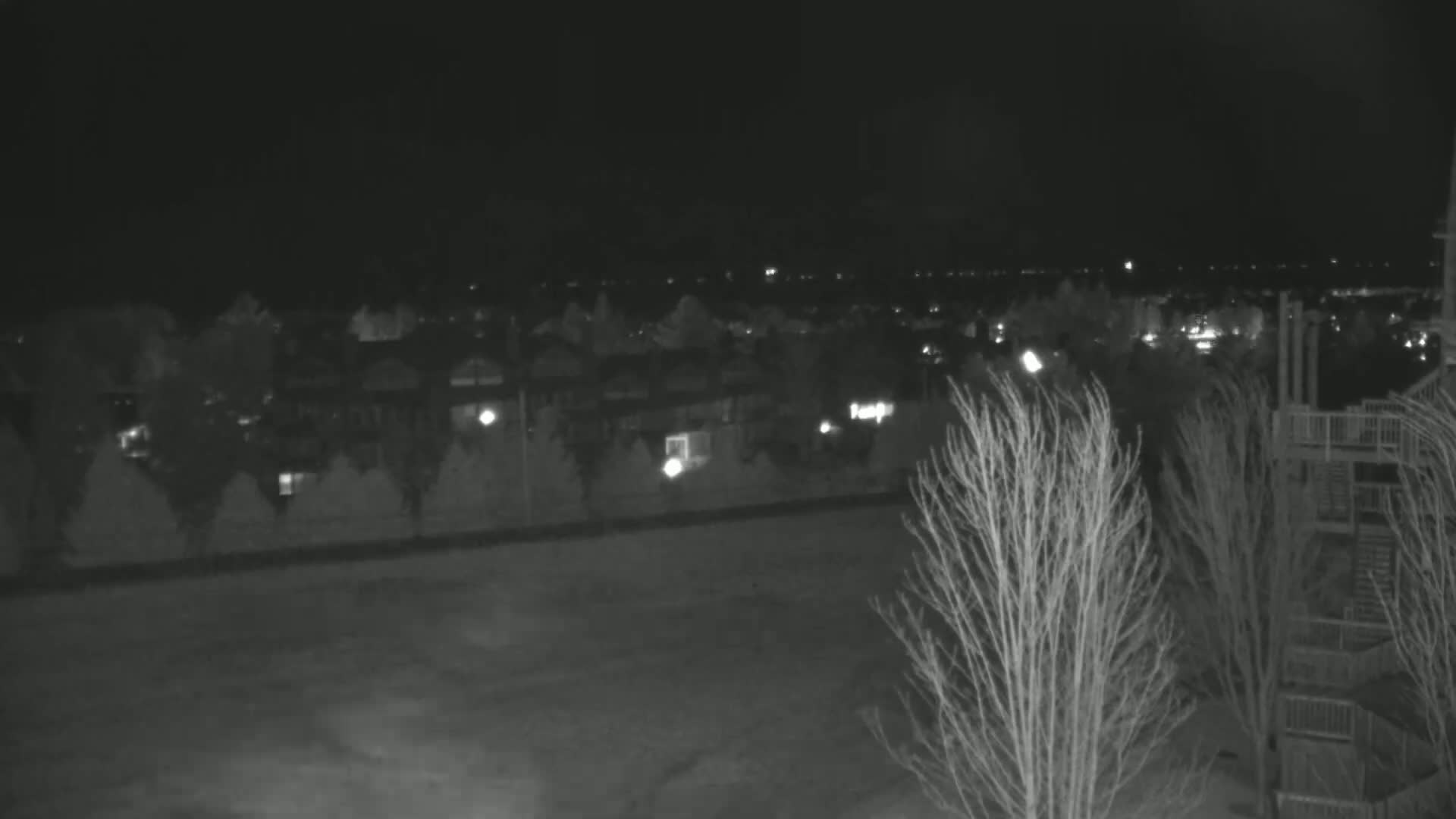 A nighttime view shows a residential area with a few lights visible, a barren tree in the foreground, and a portion of a multi-level wooden structure.