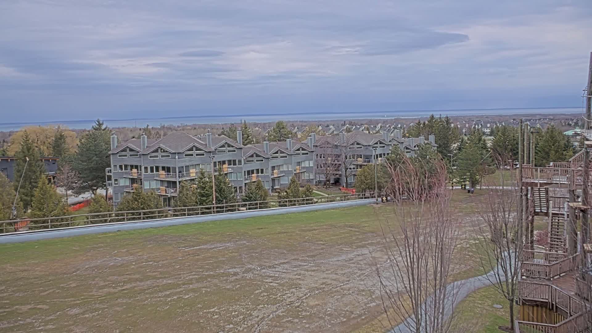 A long, gray multi-unit building sits on a hill overlooking a body of water under a cloudy sky.