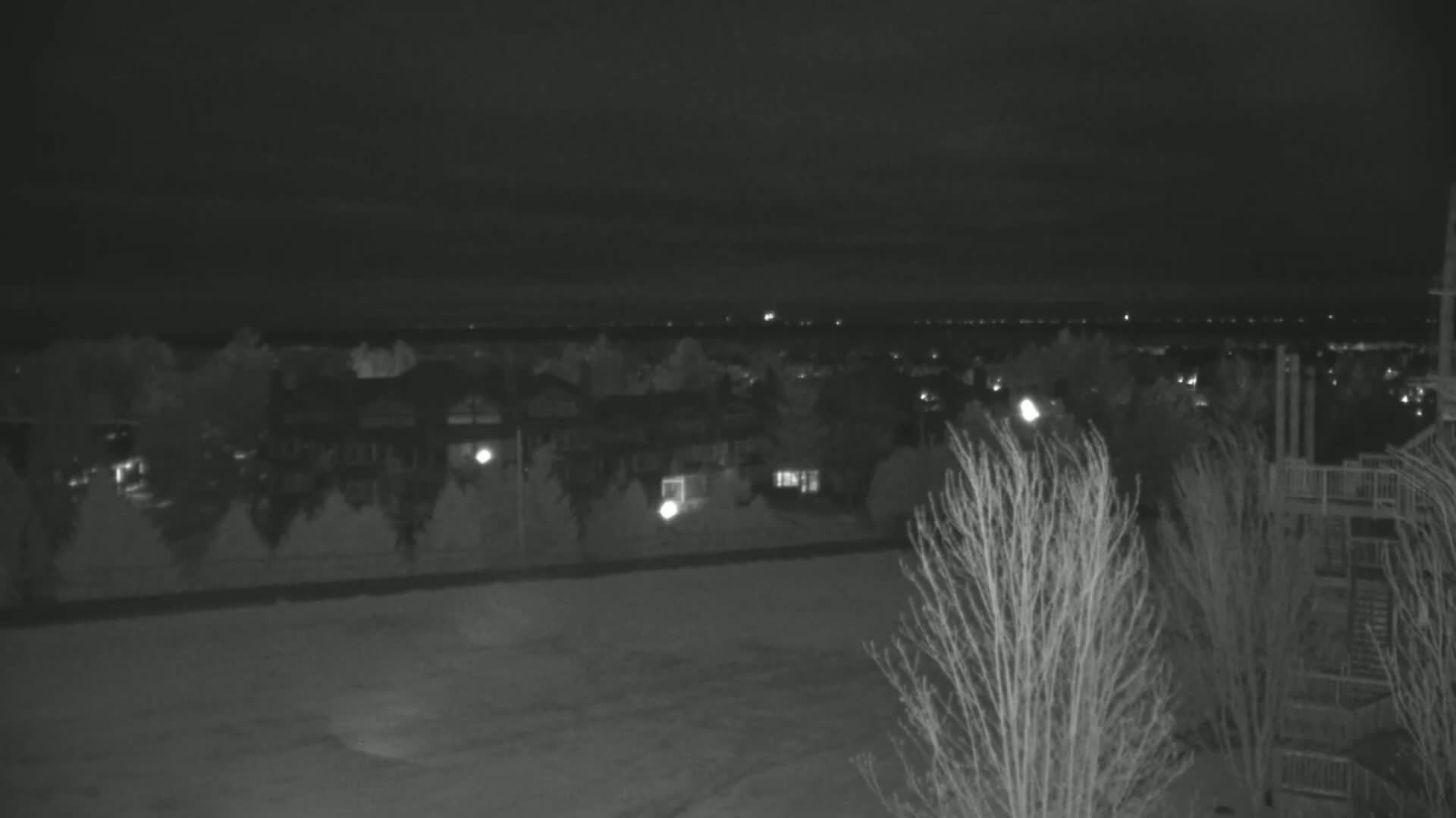 A nighttime view shows a residential area with houses and trees under a dark sky.