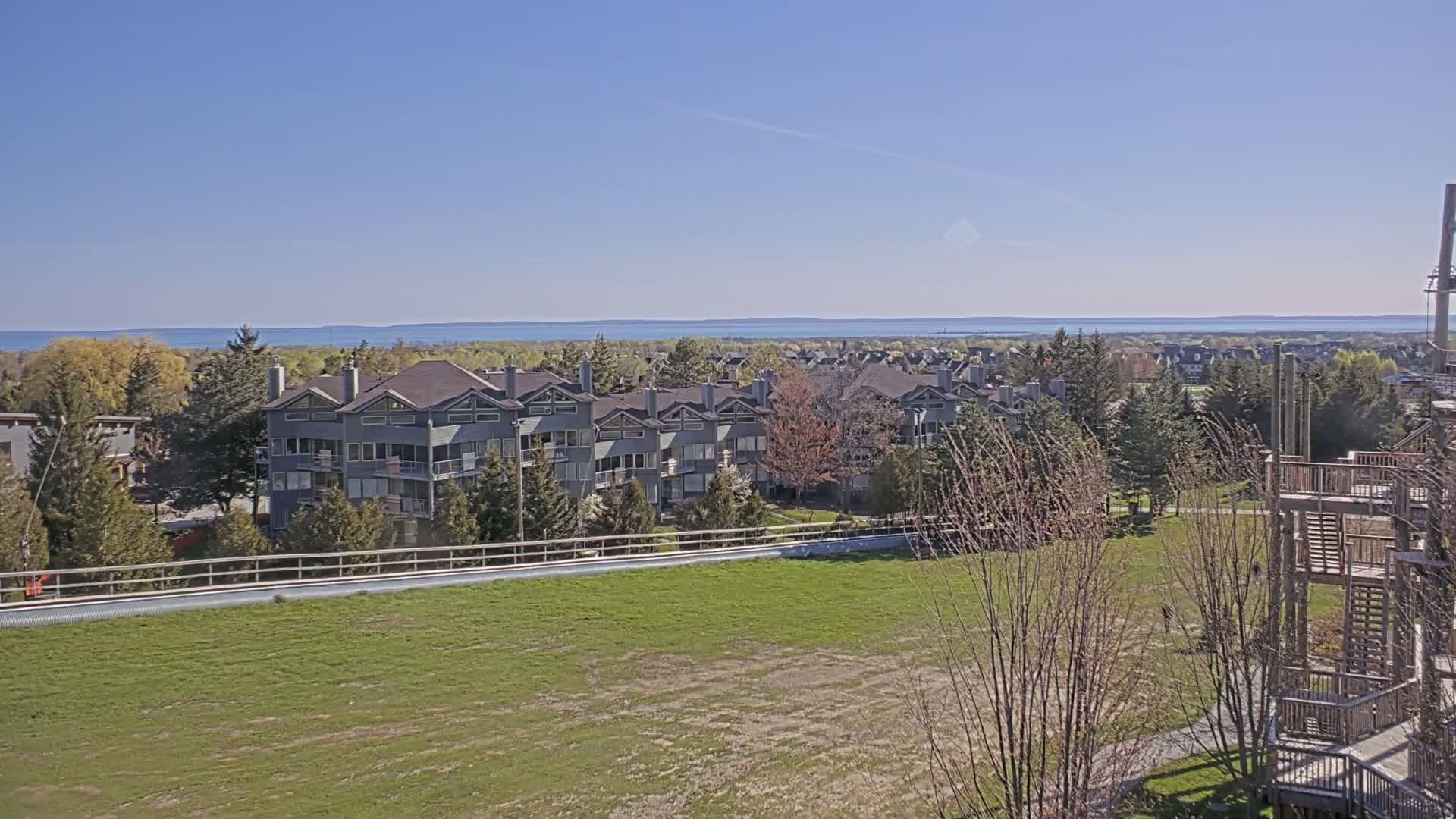 A row of gray townhouses sits on a grassy hill overlooking a calm blue lake under a clear, sunny sky.
