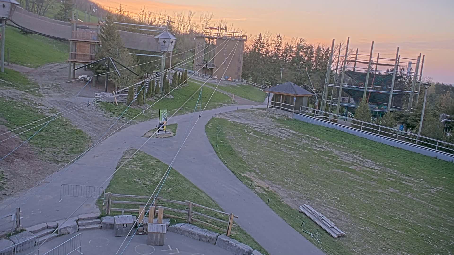 An outdoor ropes course with several platforms and zip lines is visible at sunset, with grassy areas and paved pathways connecting the structures.