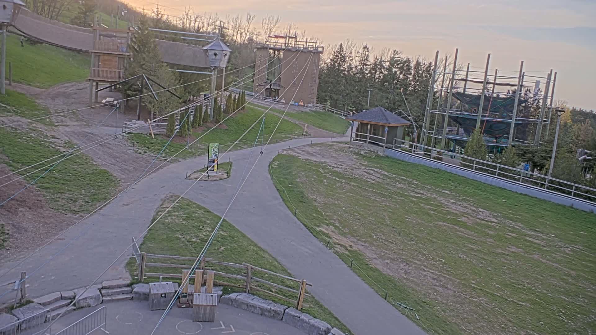 An outdoor ropes course with several platforms, zip lines, and a climbing tower is visible under a partly cloudy sunset sky.