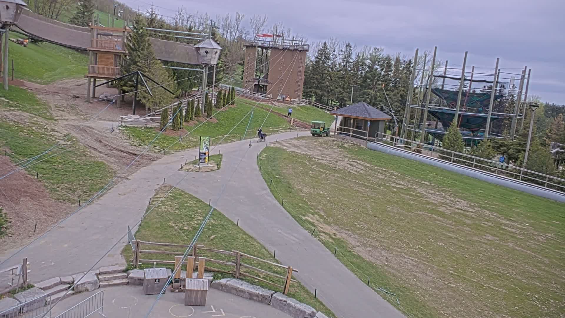 An outdoor recreational area with various structures, including elevated platforms, a climbing wall, and a ropes course, is visible under a cloudy sky.