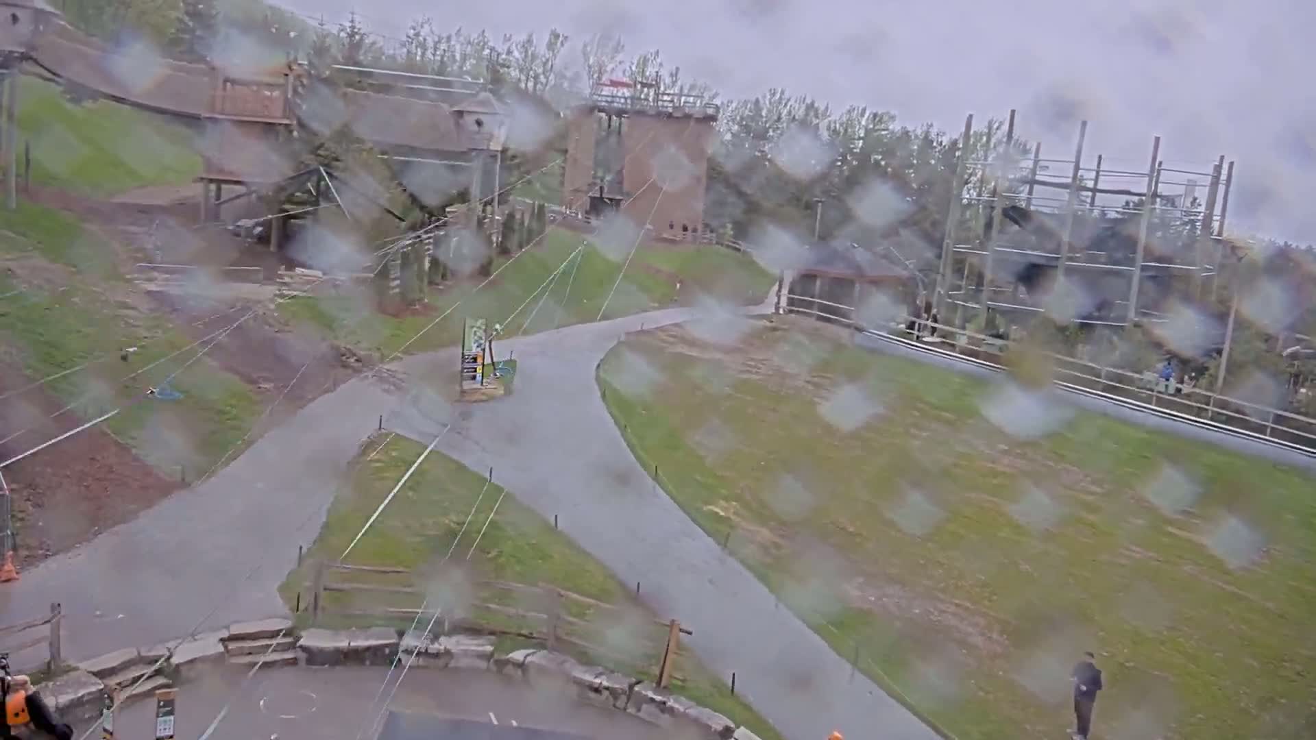 A rain-covered view of an outdoor recreational area with several elevated structures, paved paths, and grassy areas.