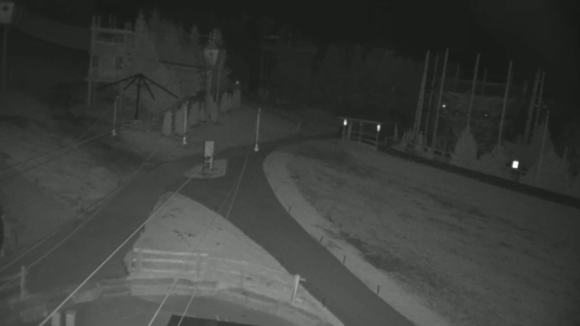 A nighttime, low-light view of a roadway intersection near a building and tall structures.