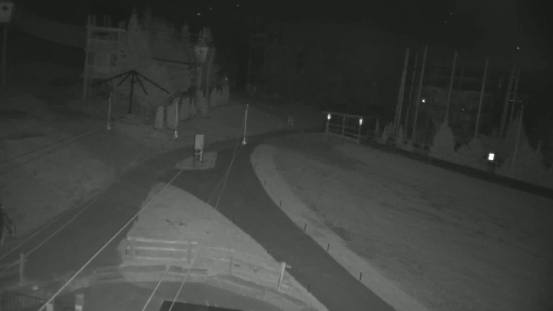 A nighttime, low-light image shows a paved road intersection near a building and a fenced area.
