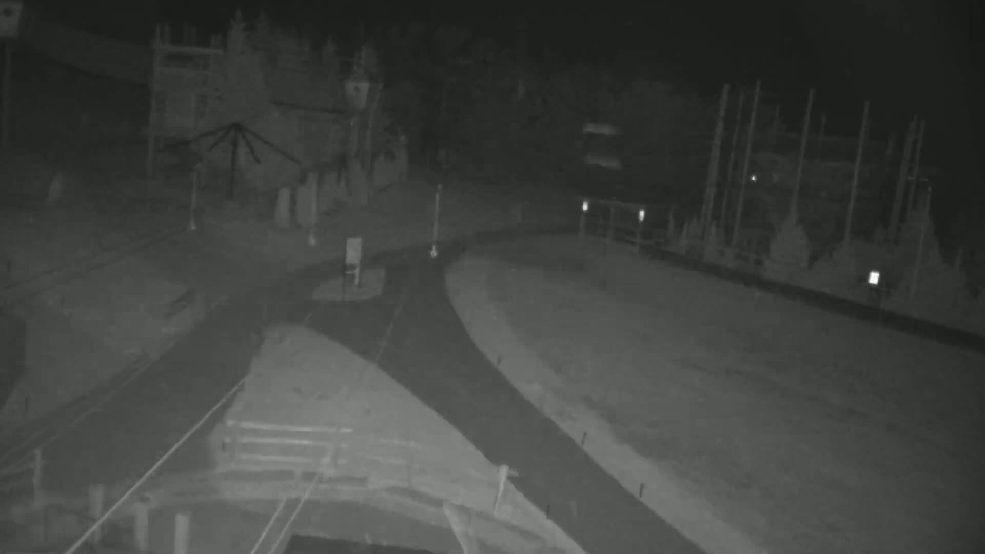 A nighttime, low-light image shows a paved area with curving paths and indistinct structures, possibly in a park or recreational area.