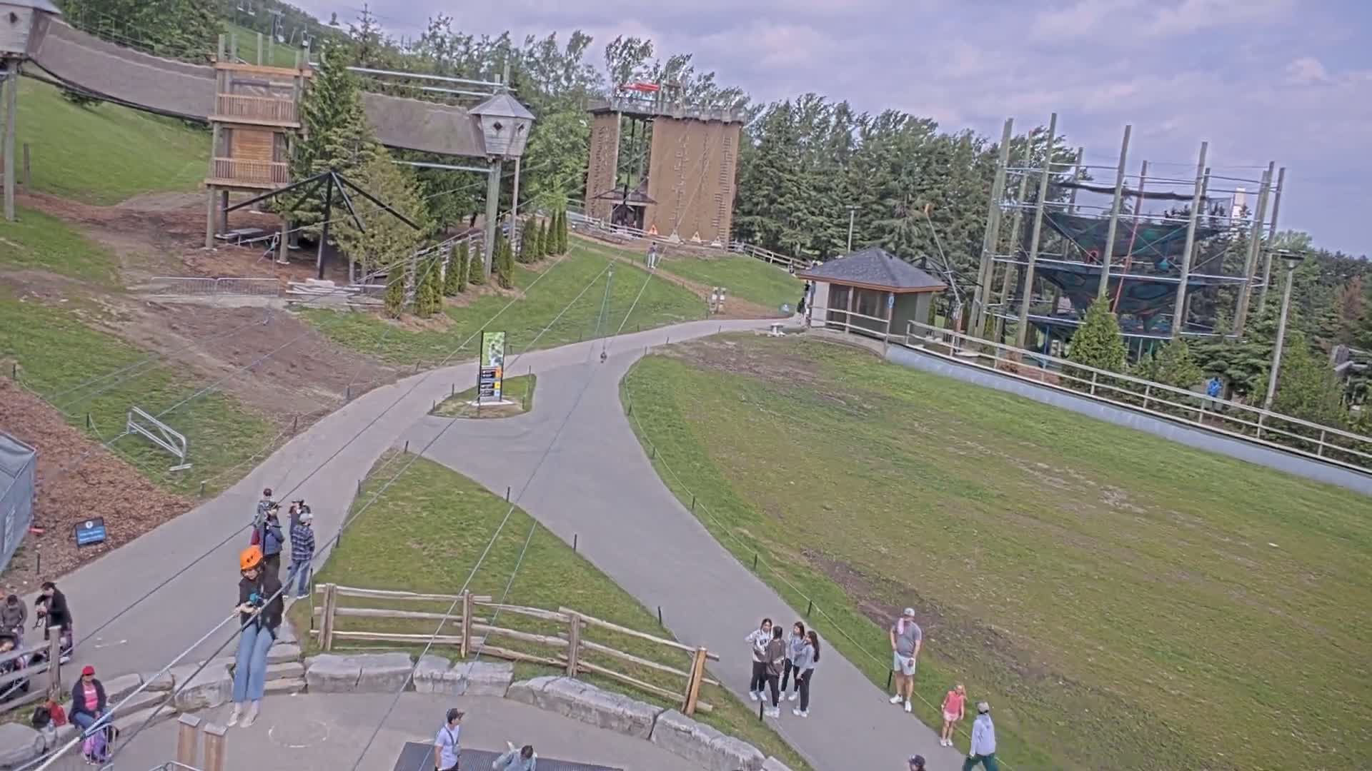 An outdoor adventure park with various climbing structures, zip lines, and walkways, under partly cloudy skies.
