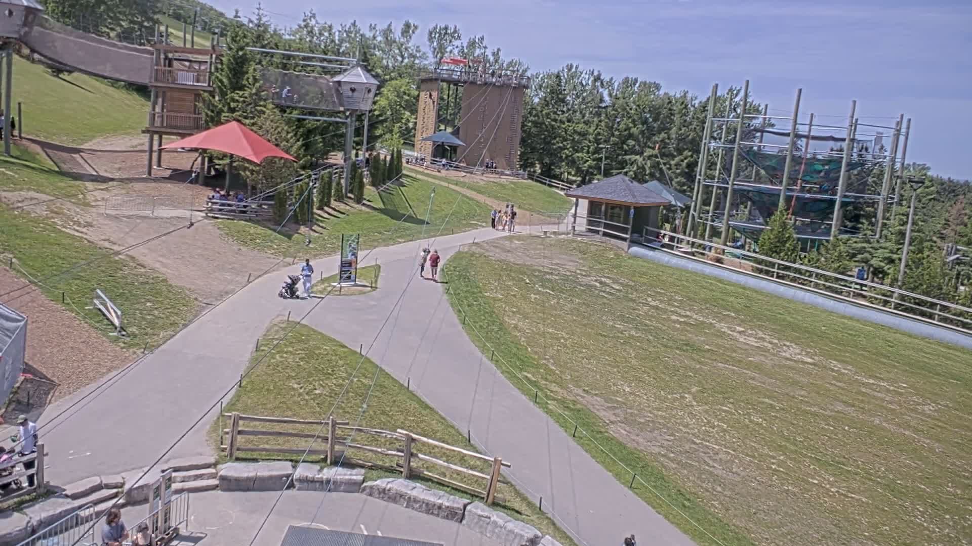 An outdoor recreational area with various climbing structures, pathways, and a red canopy under sunny skies.