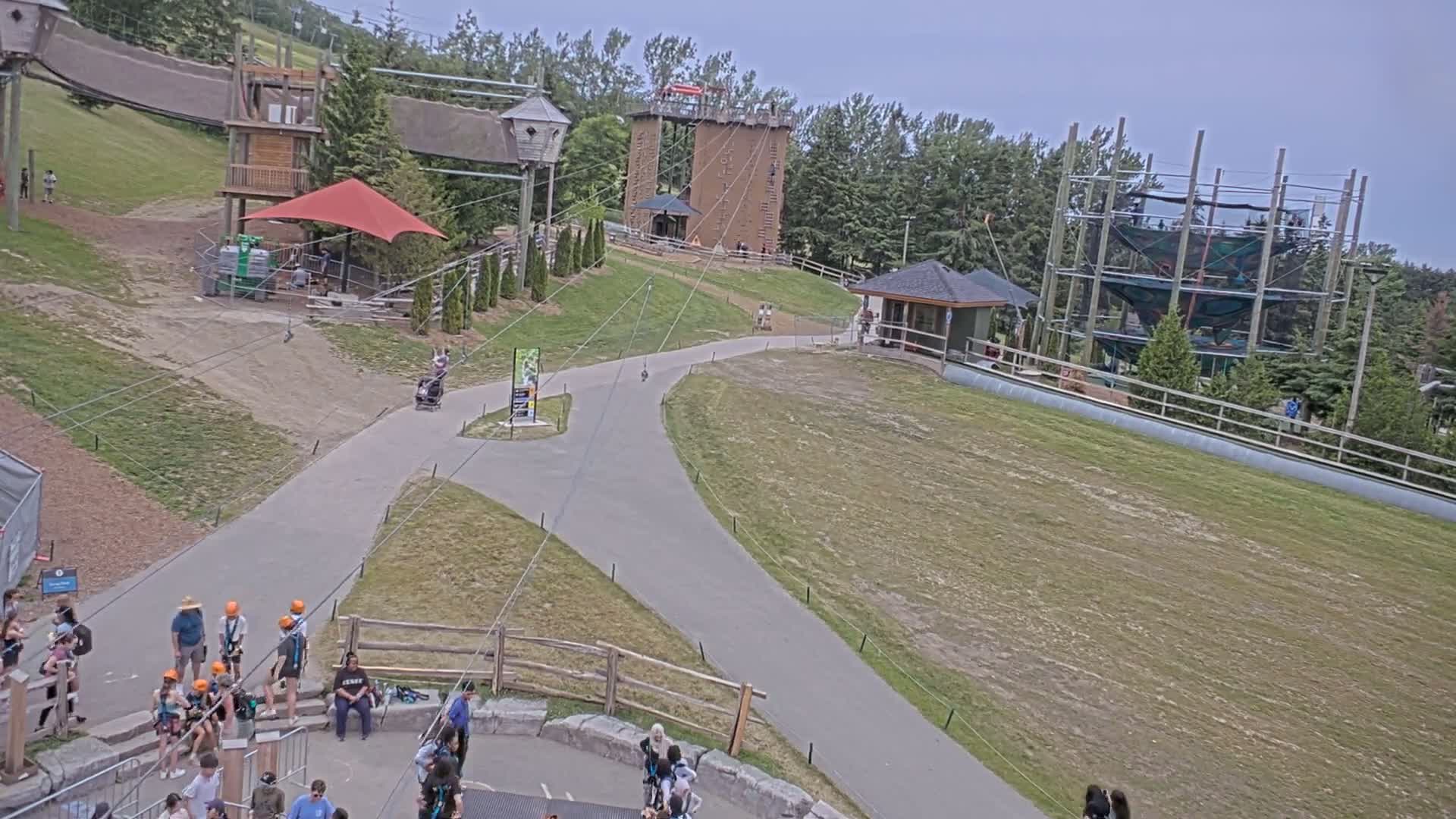 An outdoor adventure park with zip lines, climbing structures, and paved pathways, on an overcast day.