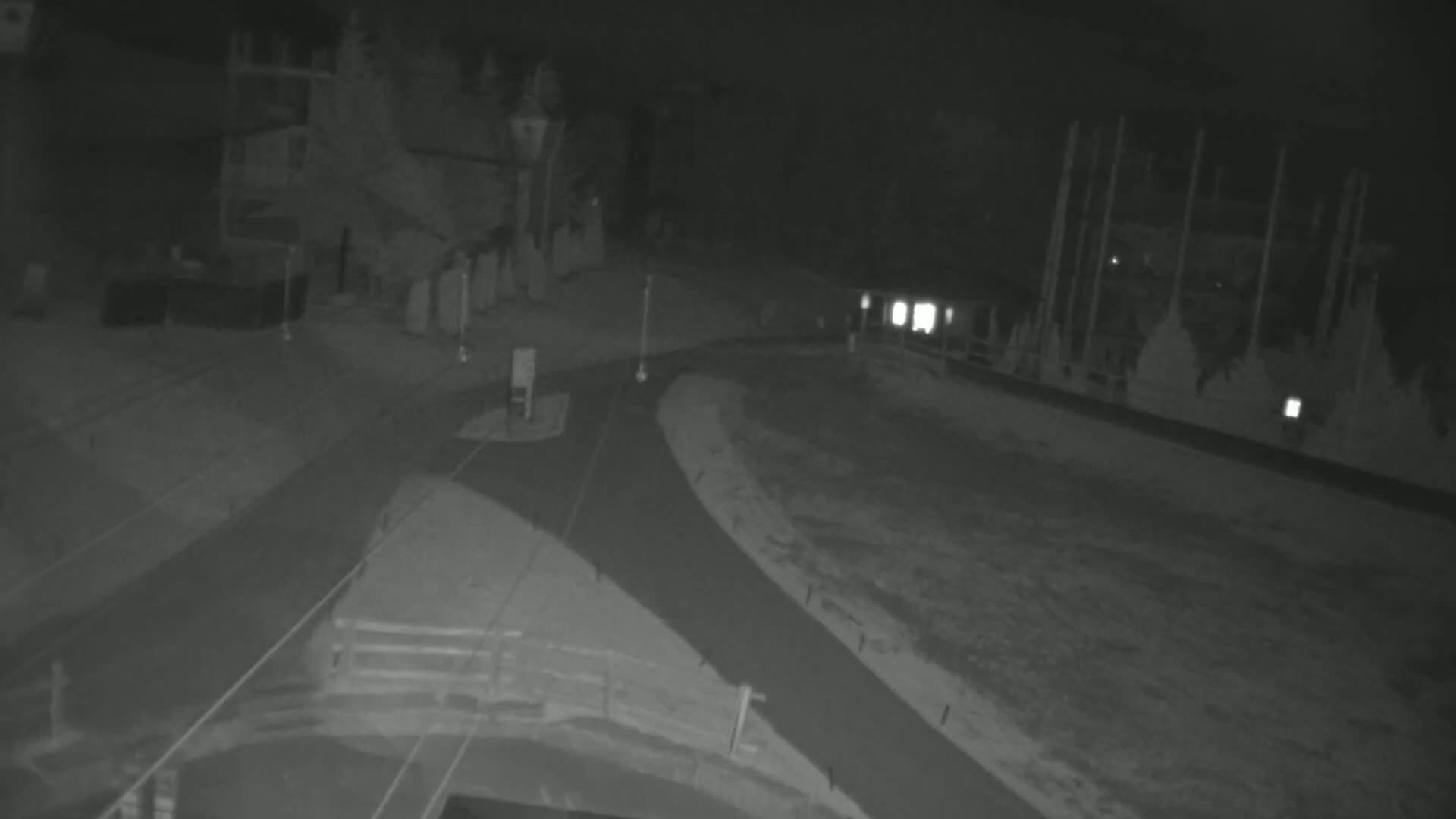 A nighttime, low-light view of a paved roadway intersecting with another road,  near some buildings and under what appears to be snowy or icy conditions.