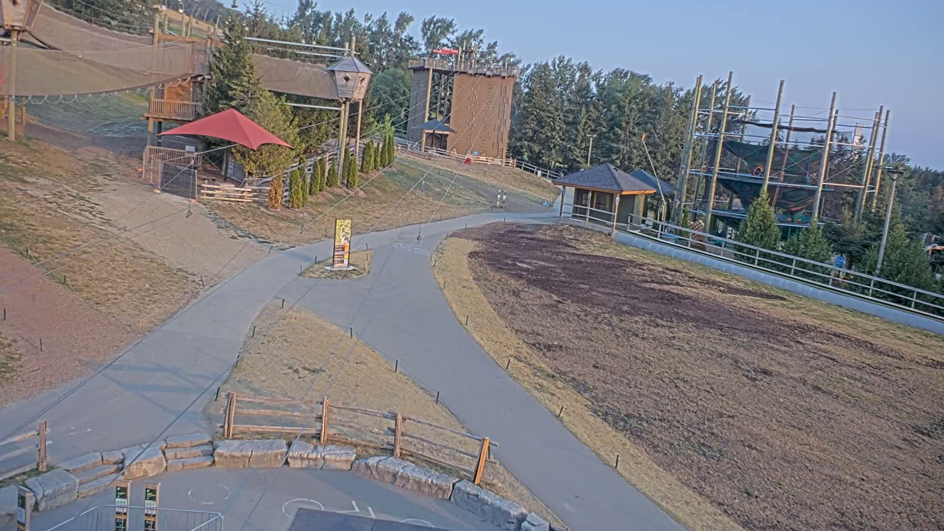 A nighttime, infrared view shows a paved road curving through a sparsely vegetated area with some structures and tall metal supports in the background.