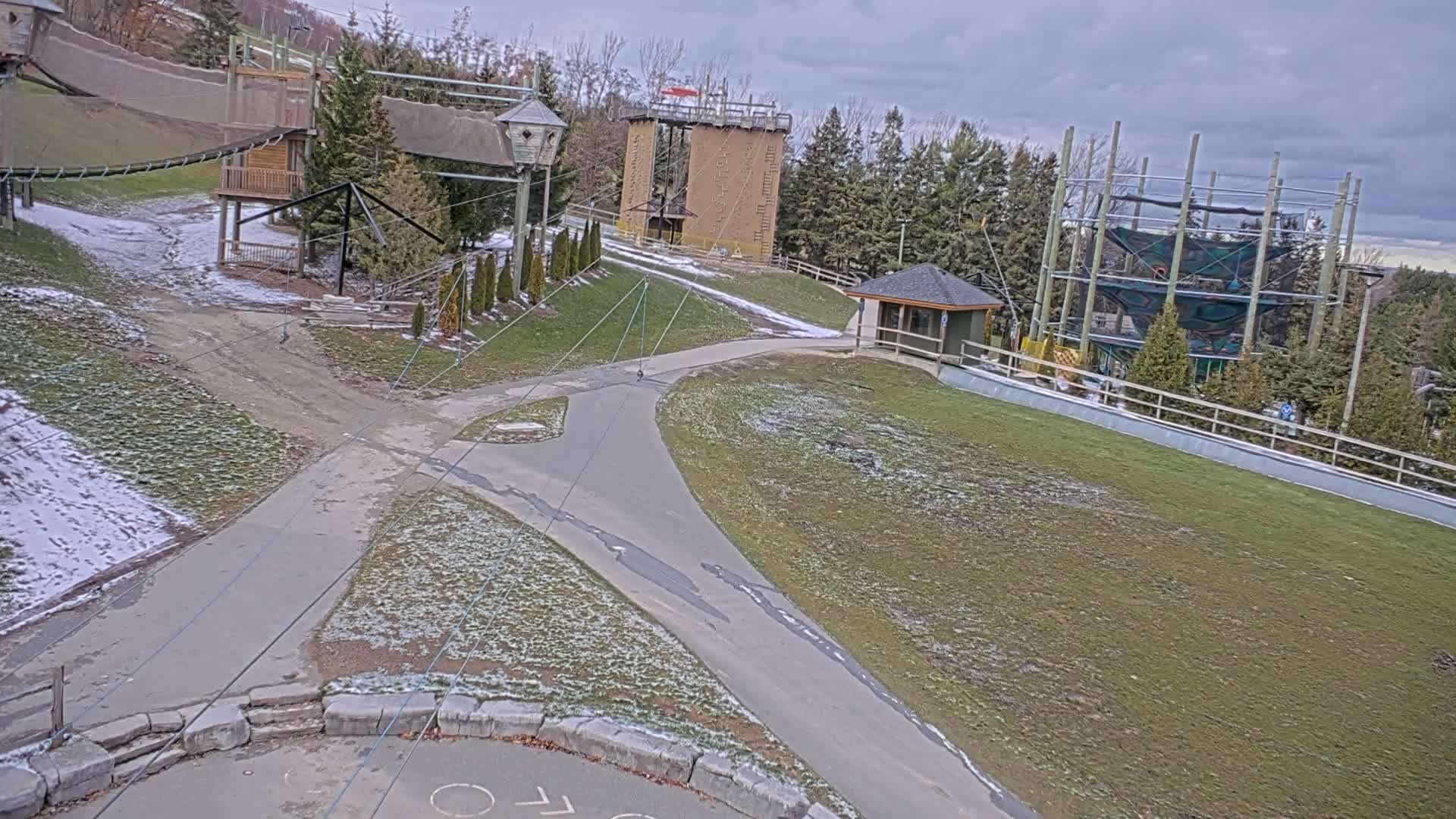 A nighttime, infrared view shows a paved road curving through a sparsely vegetated area with some structures and tall metal supports in the background.