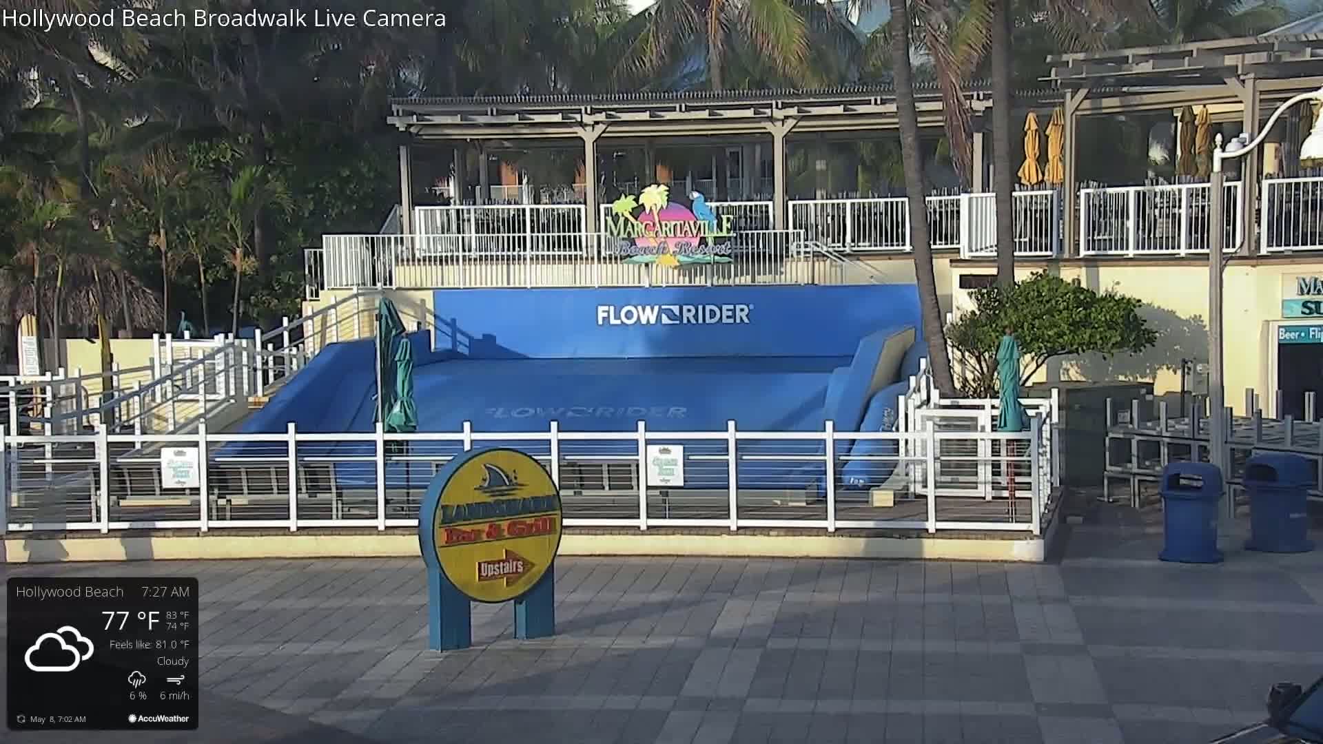 A cloudy morning shows a FlowRider surf simulator in front of a Margaritaville Beach Resort, with palm trees and other vegetation visible in the background.