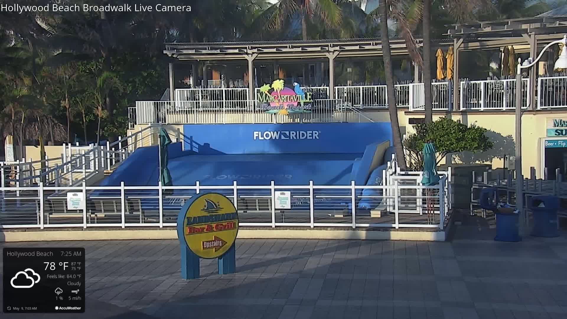 A blue FlowRider wave machine sits in front of a building on a cloudy morning.
