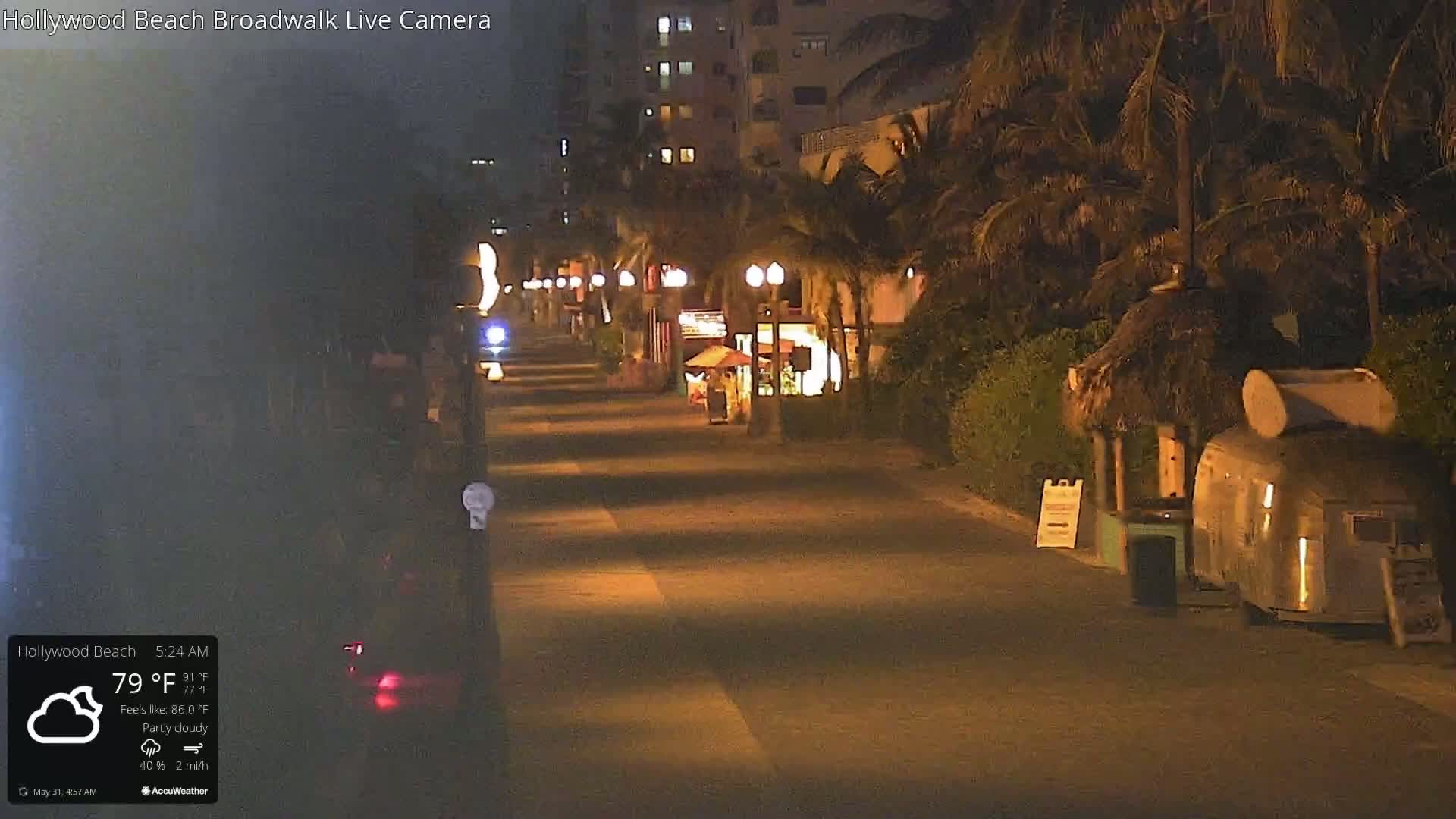 A mostly empty nighttime boardwalk, lit by streetlights, under partly cloudy skies.