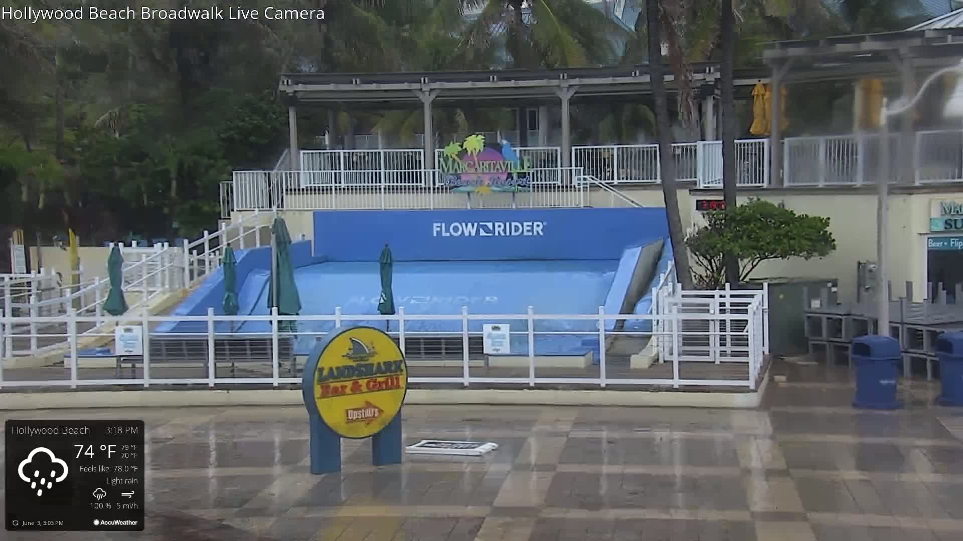 A FlowRider surfing attraction sits outside under light rain, next to a Landshark Bar & Grill.