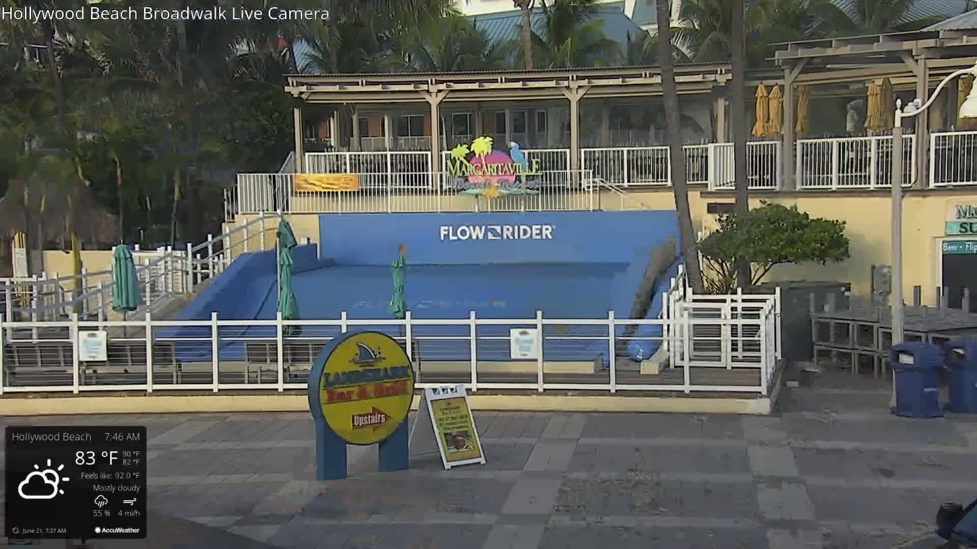A mostly cloudy morning shows a FlowRider wave machine enclosed by a white fence next to a building with a Margaritaville sign.