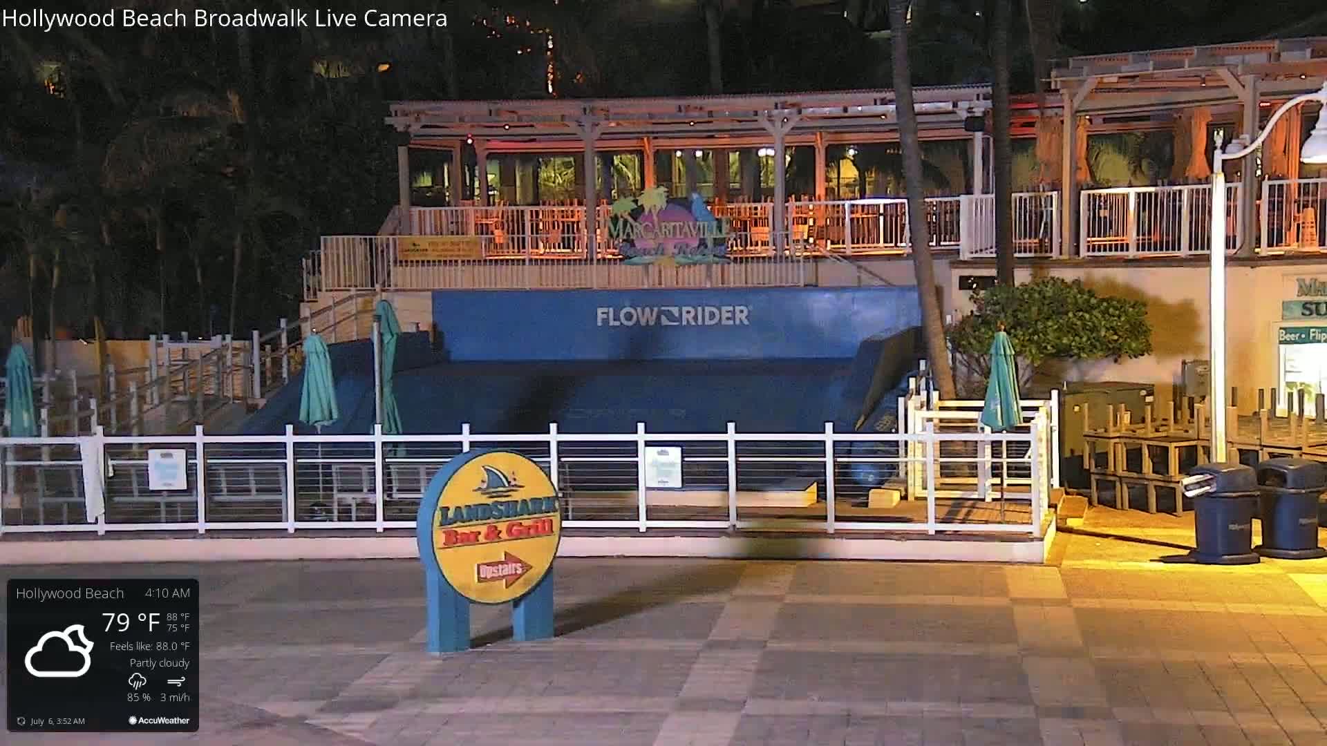 A partly cloudy night scene shows an outdoor FlowRider attraction, adjacent to a bar and restaurant, with patio furniture stacked nearby.