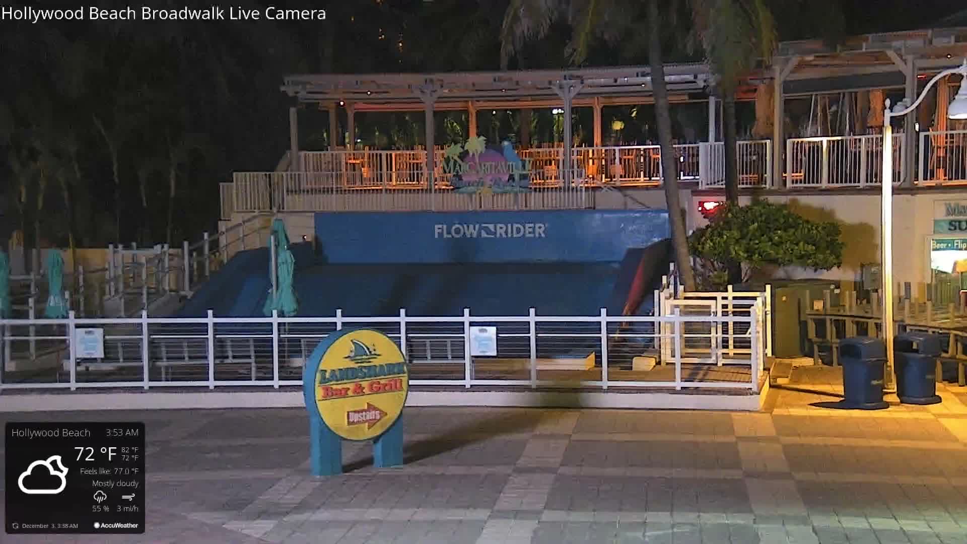 An outdoor surf simulator is visible below an illuminated elevated bar area at night, under mostly cloudy skies with a temperature of 72°F.
