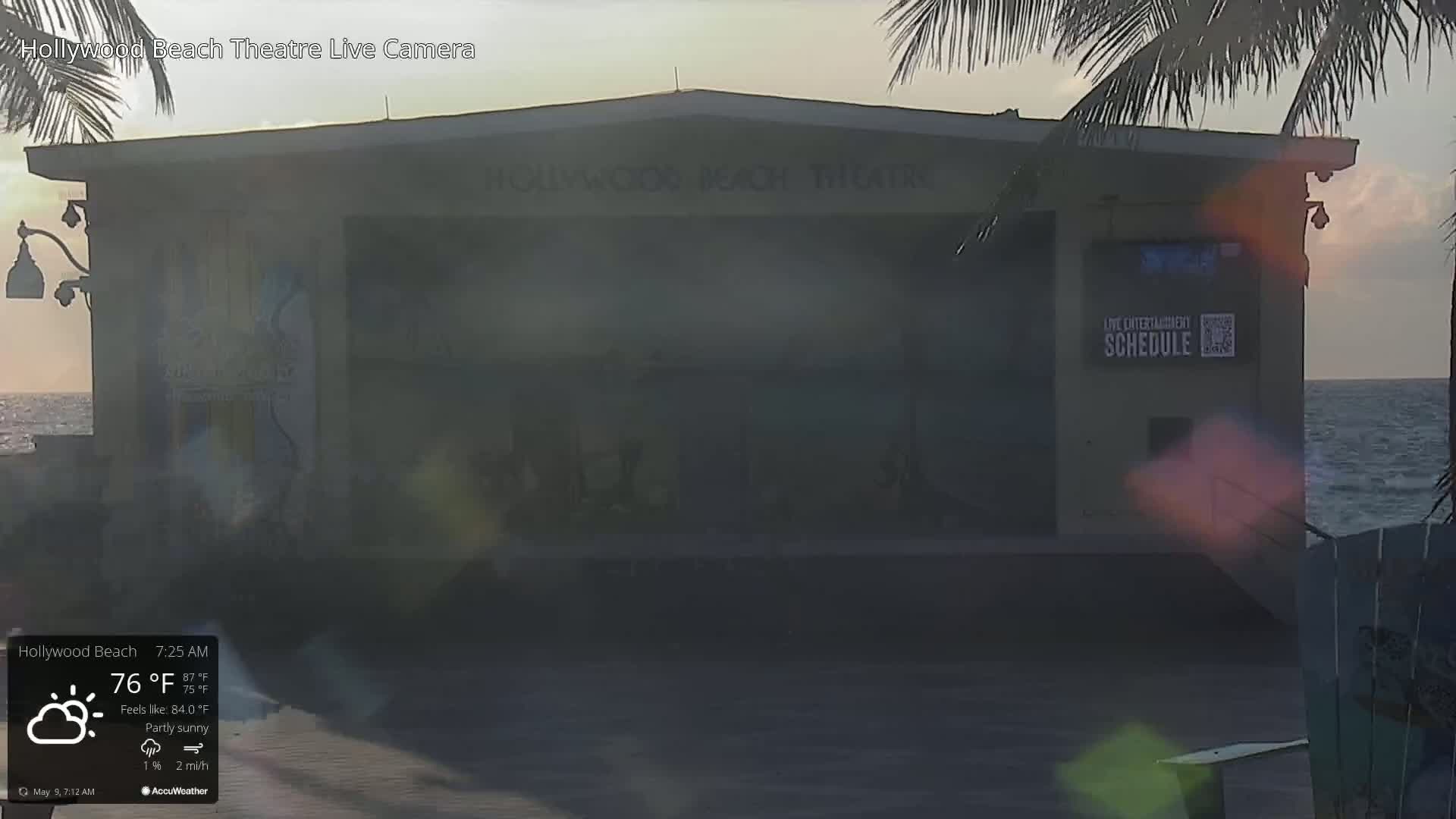 A partly sunny morning shows a beachside theater with a calm ocean in the background.