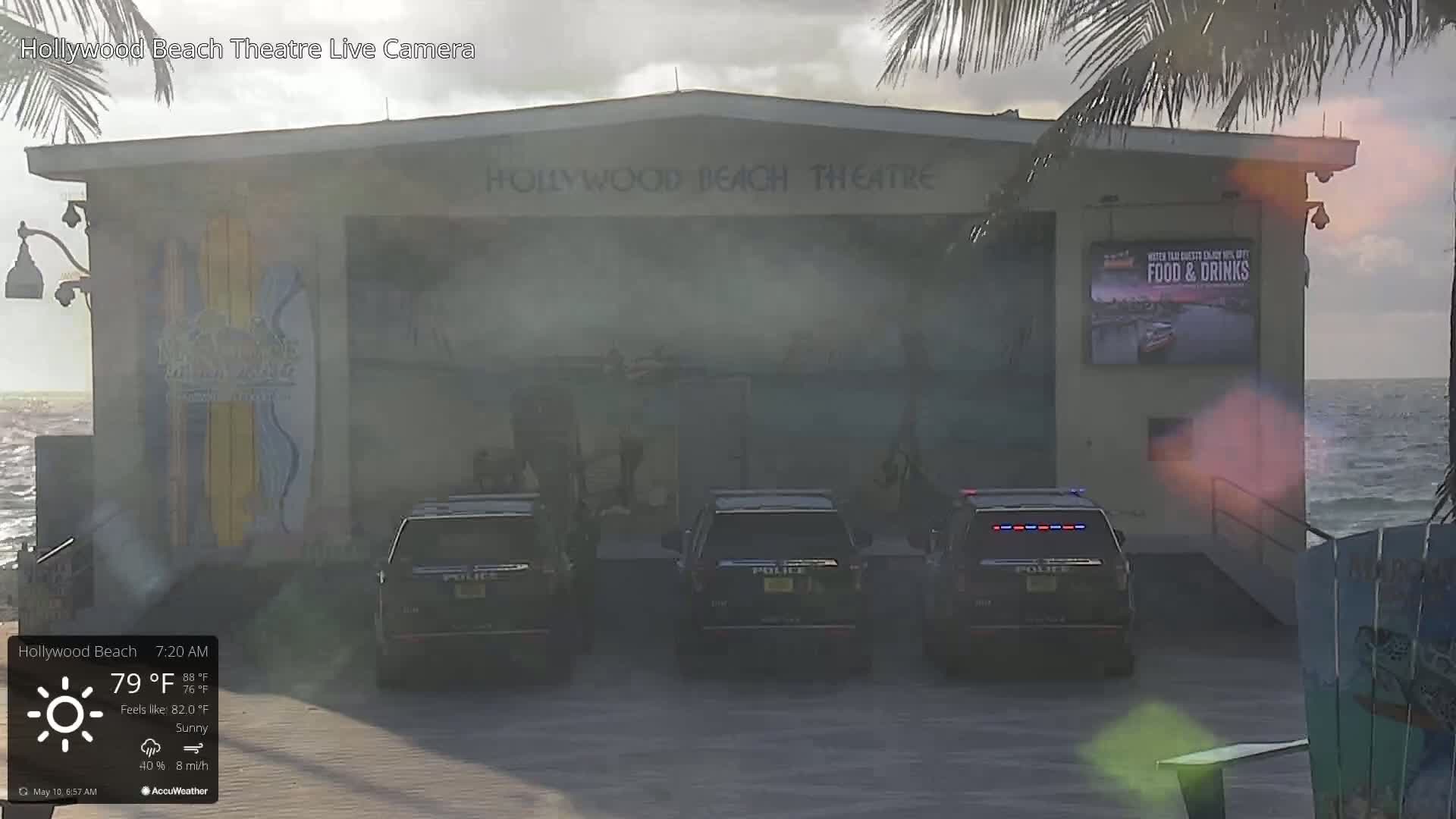Three police vehicles are parked in front of a beachside building on a sunny morning with an eight-mile-per-hour wind.