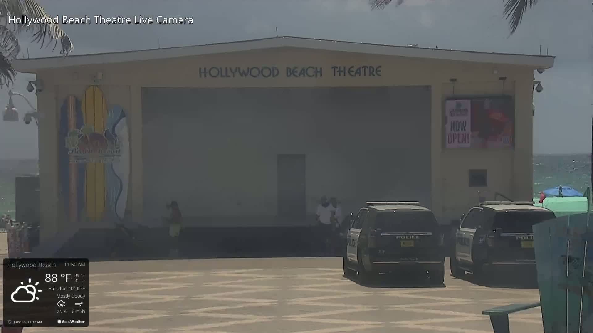A mostly cloudy, 88°F day shows the Hollywood Beach Theatre with two police SUVs parked in front, and a person walking by.