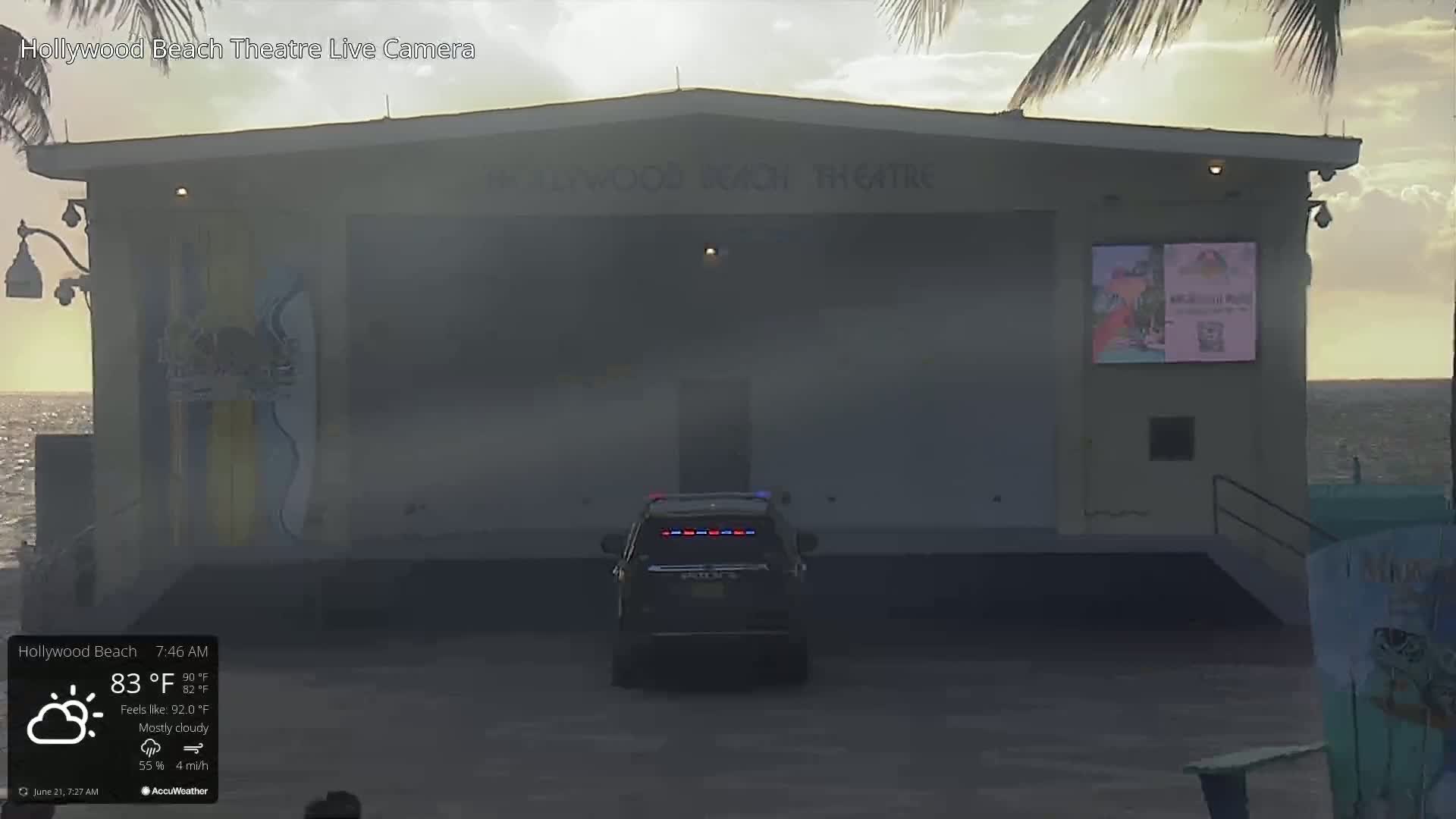 A mostly cloudy morning shows a police vehicle parked in front of a beachside theater.