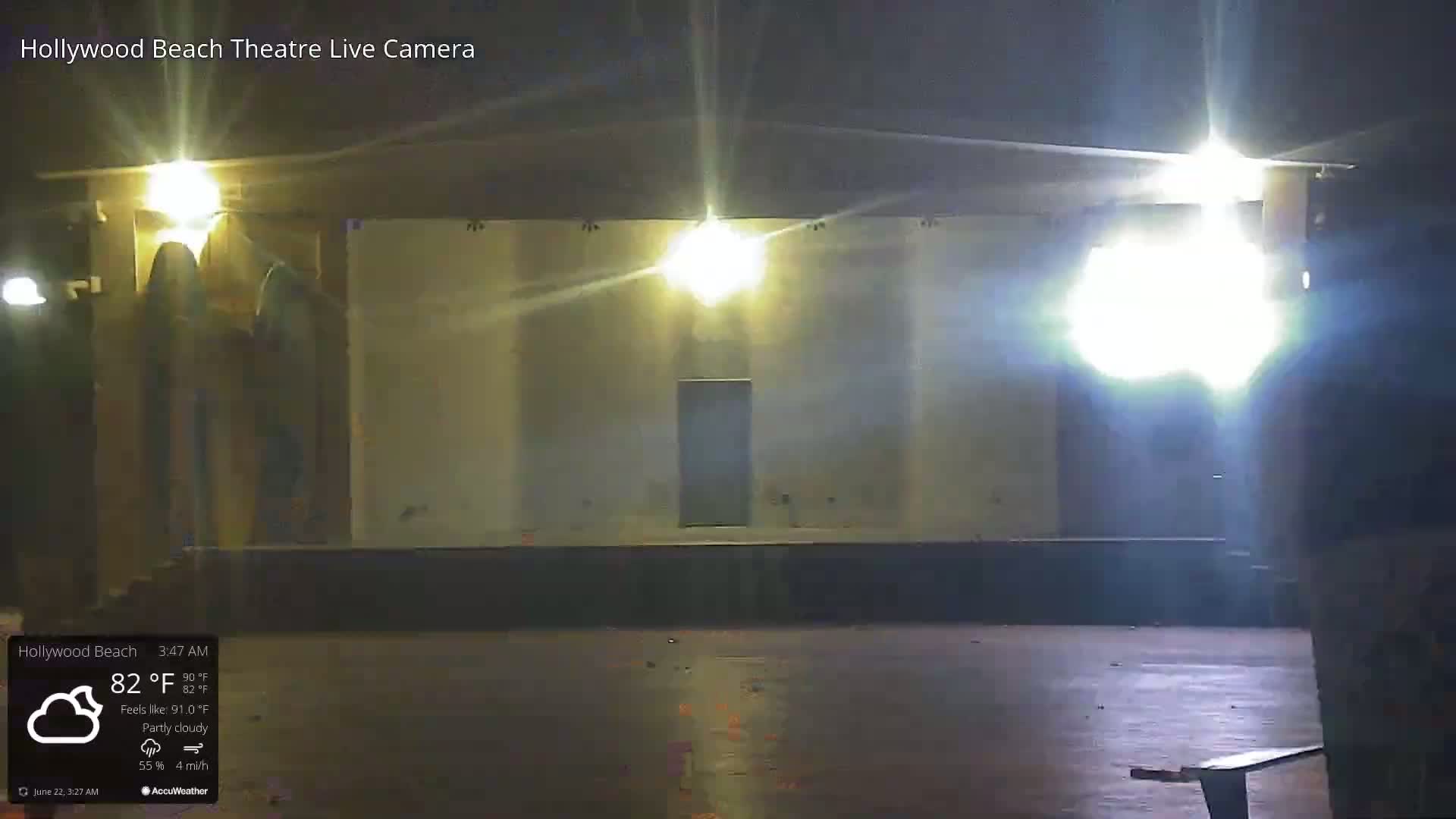 A brightly lit, empty outdoor stage is visible at night under partly cloudy conditions.