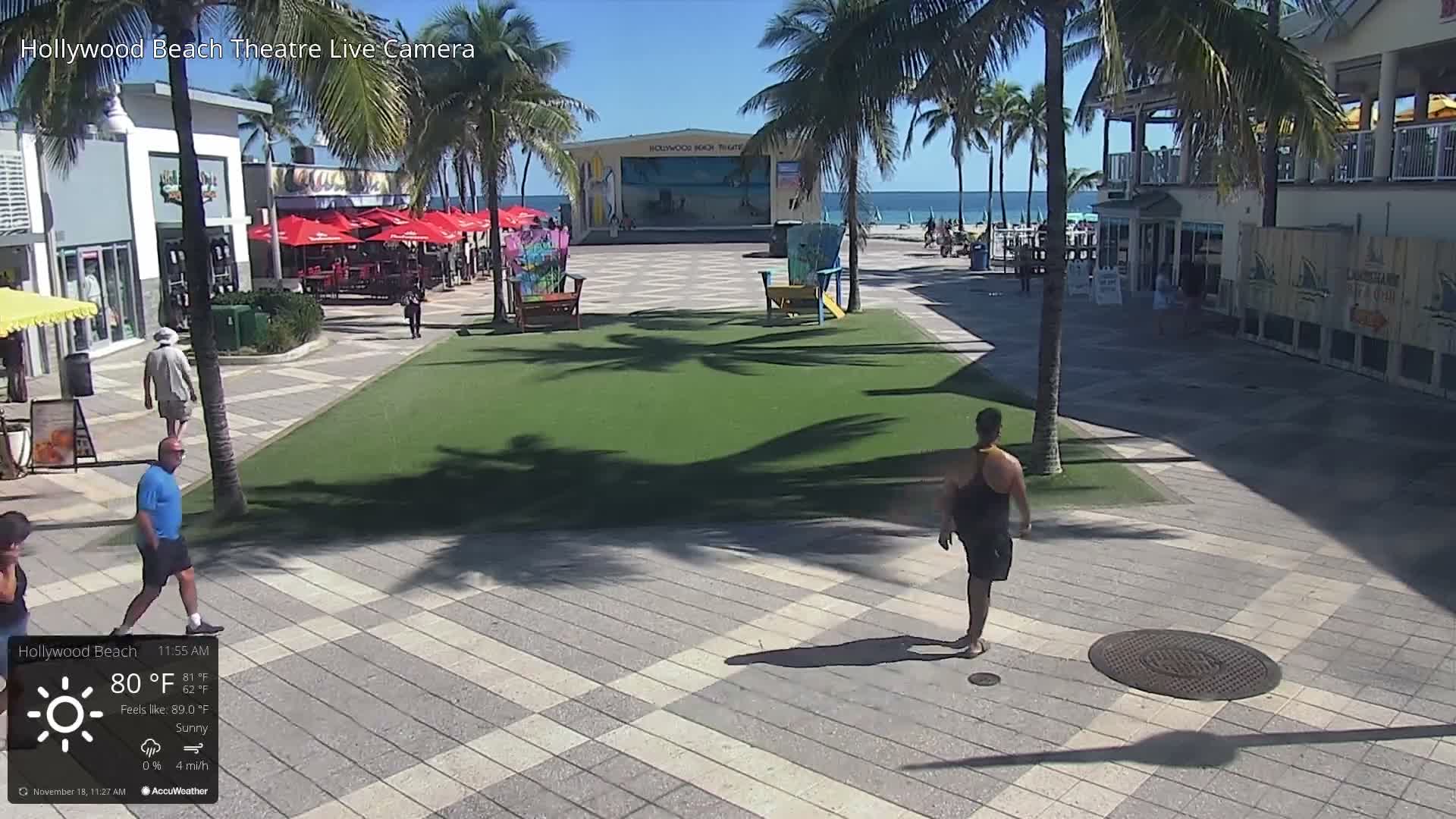 A nighttime view of an empty plaza with palm trees, buildings, and a bright light source in the center under partly cloudy skies.