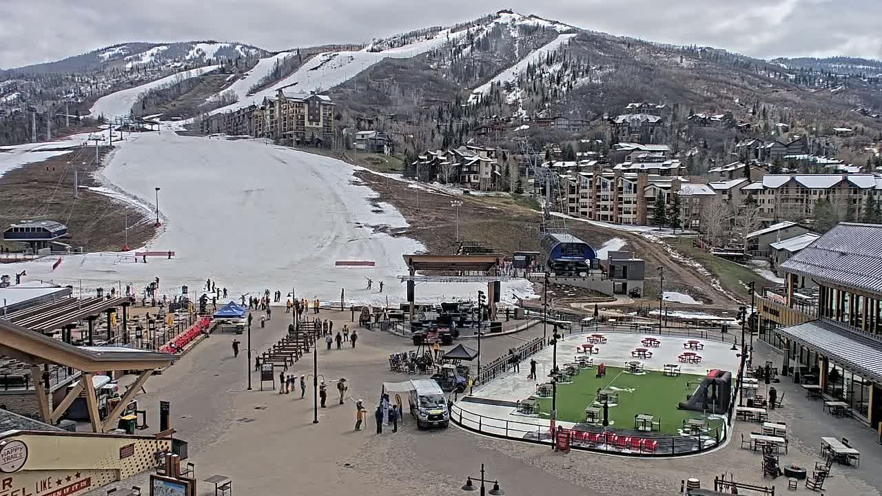 A snow-covered ski slope and resort base area with people are visible under a cloudy sky.