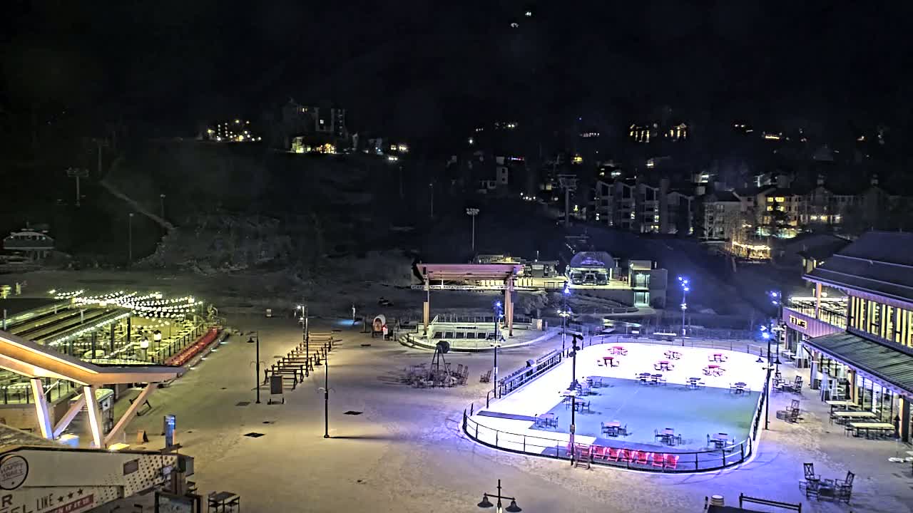 A brightly lit outdoor ice rink surrounded by buildings and snow-covered ground at night.