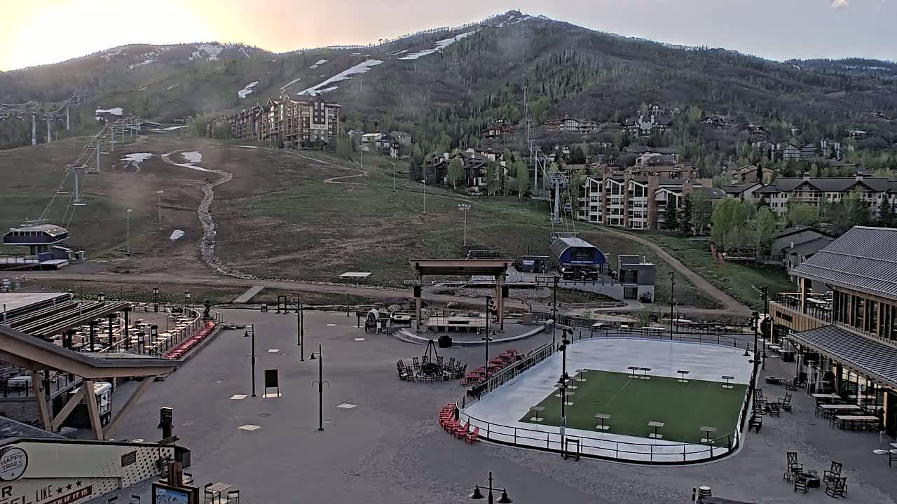 A mountainside resort village with an outdoor skating rink and seating areas is visible under a partly cloudy, dusky sky.