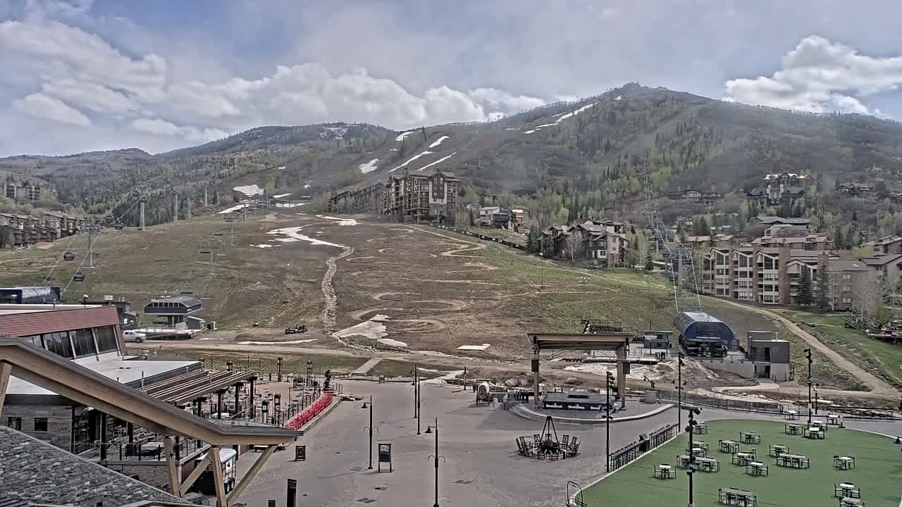 A brightly lit, snow-covered mountain ski resort village is captured at night, showcasing illuminated buildings, ski slopes with lifts, an outdoor dining area, and an ice rink on a cold, dark evening.