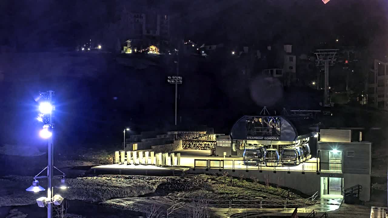 A gondola station with several gondolas is illuminated at night under a dark, possibly rainy sky.