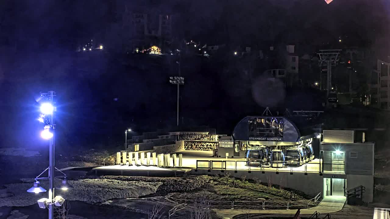 A gondola station with several gondolas is illuminated at night, under a dark, possibly cloudy sky.