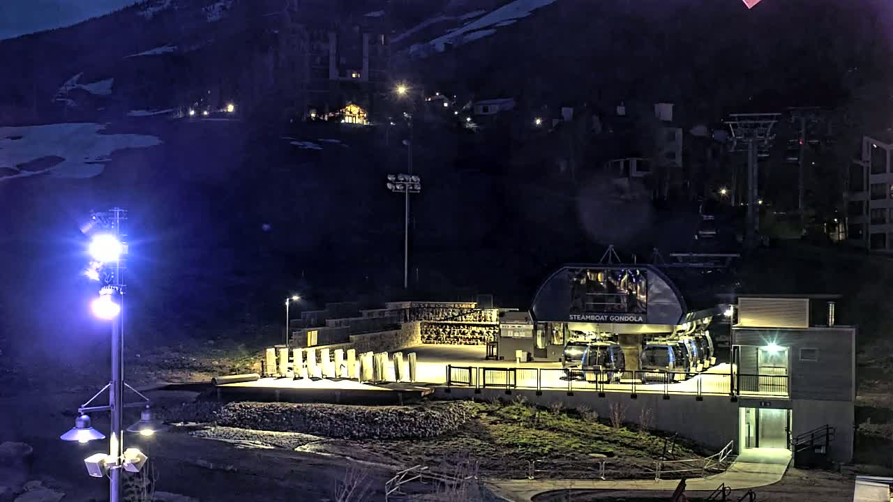 A gondola station at night on a snow-dusted mountainside, illuminated by artificial lights.