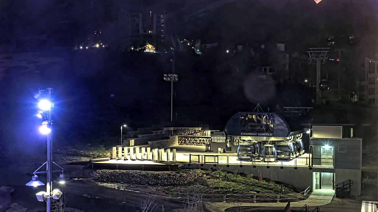A gondola station sits at the base of a dark, snow-covered mountain at night, illuminated by artificial lights.