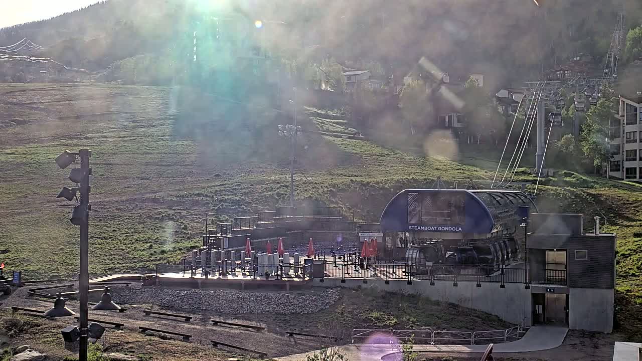 A gondola station sits at the base of a grassy hillside on a hazy, sunny day.