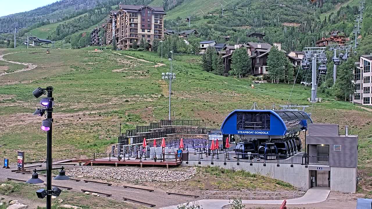 A gondola station sits at the base of a mountain, with several buildings and chairlifts visible uphill.