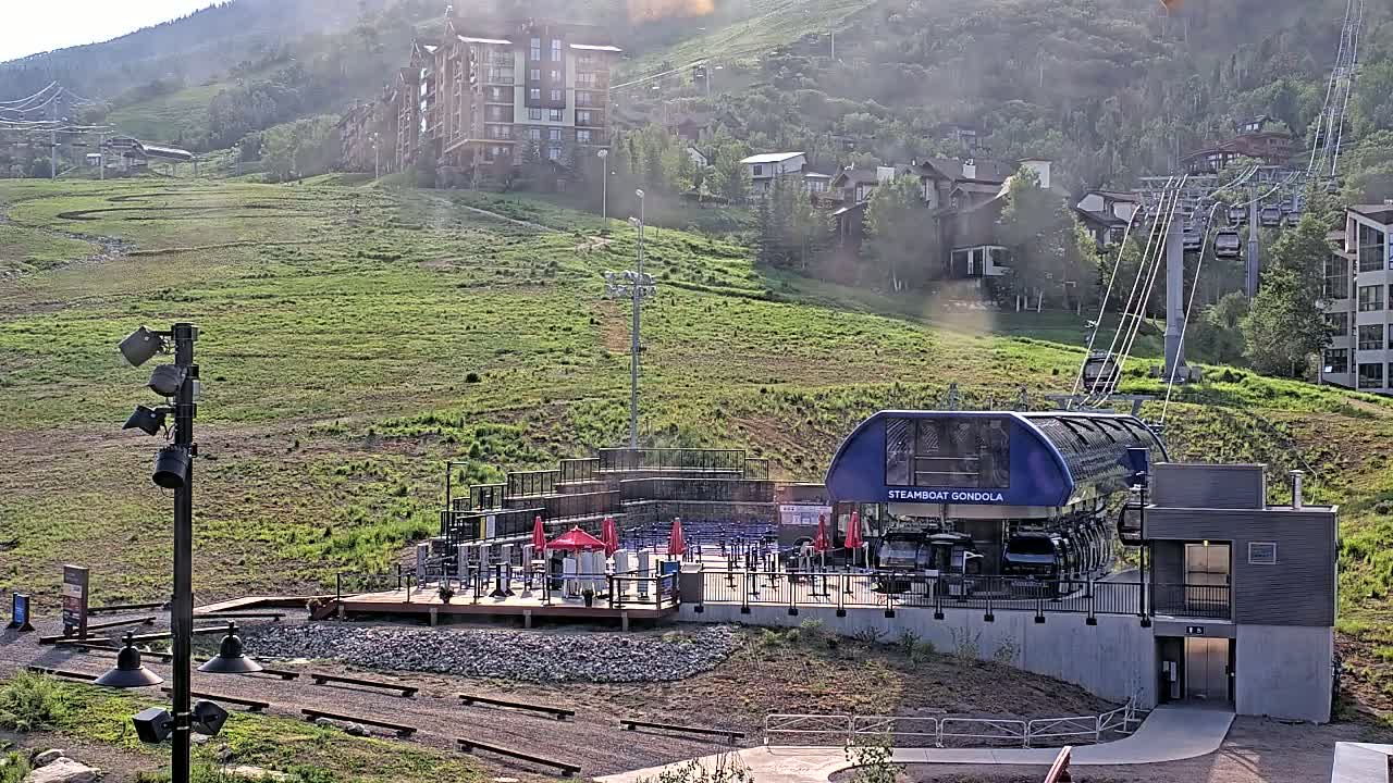 A gondola station sits on a grassy hillside overlooking a residential area on a hazy, sunny day.